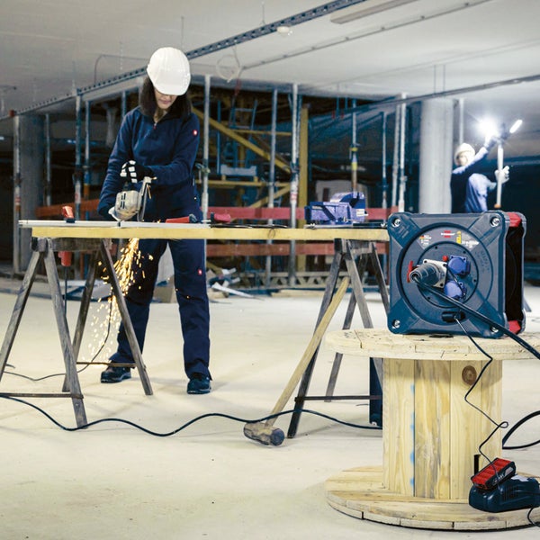 Arbeitsszene auf einer Baustelle mit einer Person, die mit einer Flex arbeitet und einem Kabelaufroller