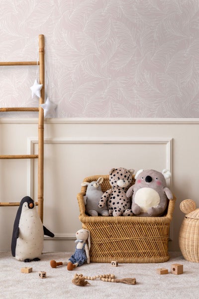 Helles Kinderzimmer mit weißem Schreibtisch vor einer hellrosa Tapete mit weißem Federmuster. Auf dem Tisch stehen eine Lampe und Spielzeug.