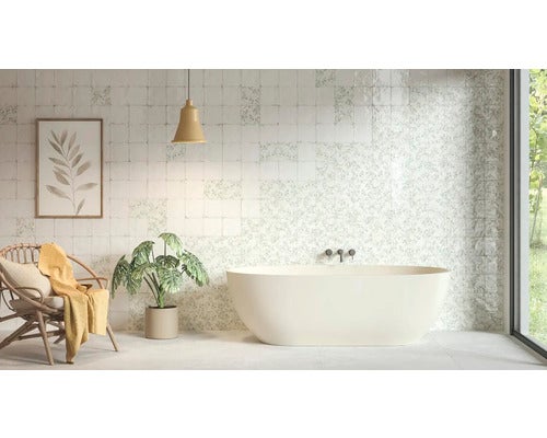 Modernes Badezimmer mit freistehender Badewanne vor einer Wand aus weiß-gemusterten quadratischen Fliesen, einem Korbstuhl und einer Zimmerpflanze.