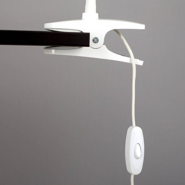 Weiße Klemmleuchte mit Befestigungsclip an einer Platte und Schnurschalter am Kabel.