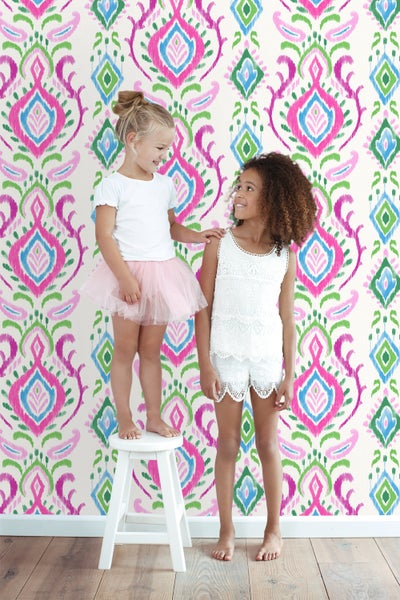 Zwei Mädchen vor einer Wand mit einem farbenfrohen Muster aus Rauten und floralen Elementen