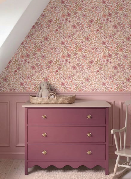 Blumentapete mit dichten Blüten und Blättern in einem Kinderzimmer über einer rosa Wandvertäfelung und einer Kommode.