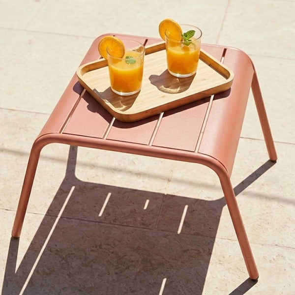 Kleiner Gartenbeistelltisch aus Metall mit einer Tischplatte aus Lamellen, darauf ein Holztablett mit zwei Gläsern Saft.