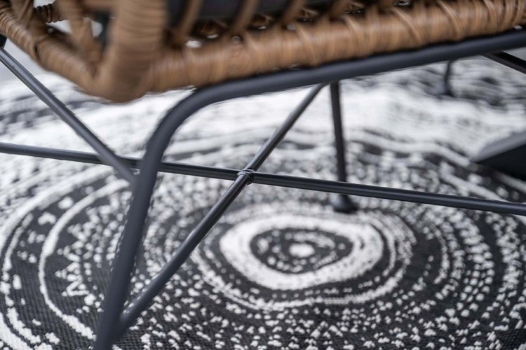 Nahaufnahme eines schwarzen Metallgestells eines Stuhls mit braunem Geflecht auf einem gemusterten Teppich.