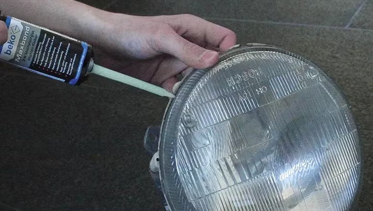 Eine Person trägt mit einer Kartuschenpistole Beko Maxbond Kleber auf den Rand eines runden Autoscheinwerfers auf.