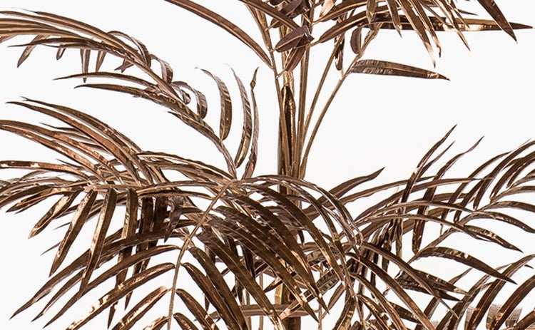 Künstliche Palme mit goldfarbenen Stämmen und Blättern in einem schwarzen Topf.