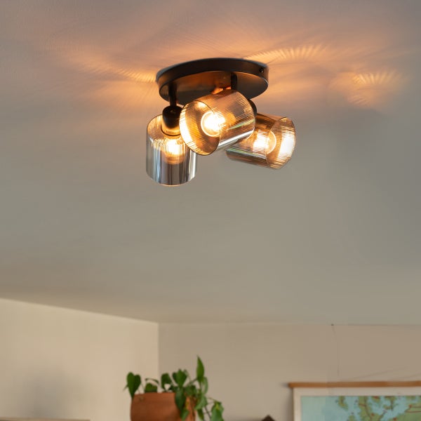 Dreiflammige Deckenleuchte mit geriffelten Glasschirmen und Metallsockel in einem hellen Raum mit modernem Design.