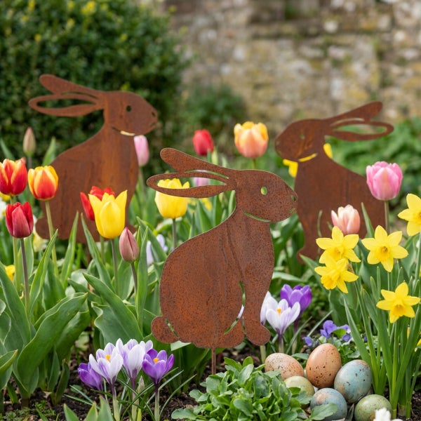 Drei Hasen Silhouetten aus Edelrost zur Dekoration in einem frühlingshaften Blumenbeet mit Tulpen und Krokussen.