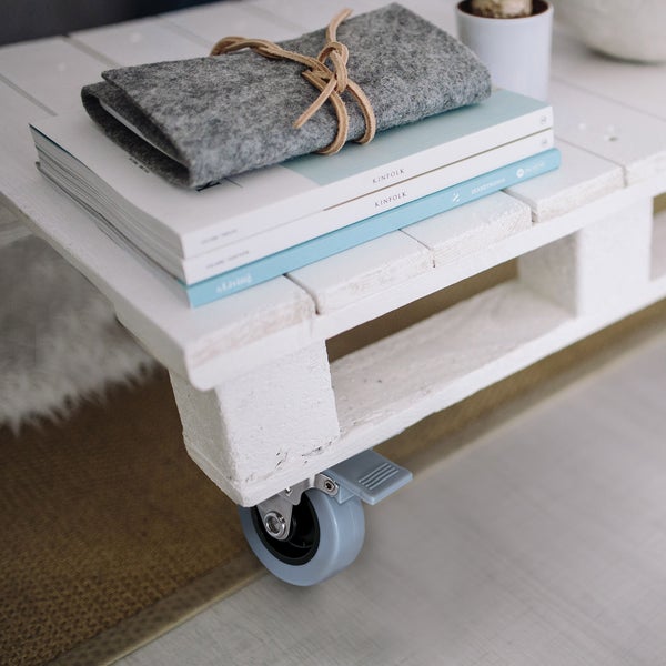 Couchtisch aus weißer Holzpalette mit Lenkrolle und Feststeller, dekoriert mit Büchern und einer Filztasche.