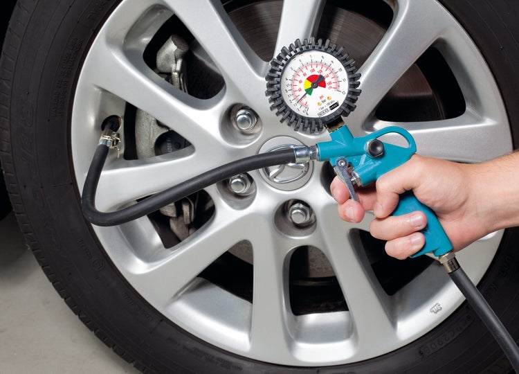 Hand mit Arbeitshandschuh setzt ein Reifenfüll-Anschlussstück auf das Ventil eines Motorradreifens.