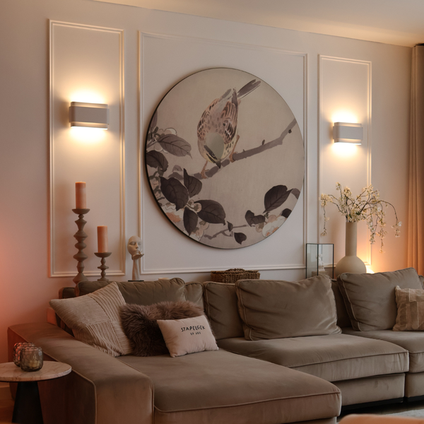 Hell gestaltetes Wohnzimmer mit beigem Sofa, runder Wanddekoration mit Vogelmotiv zwischen zwei modernen Wandleuchten und stilvoller Dekoration.