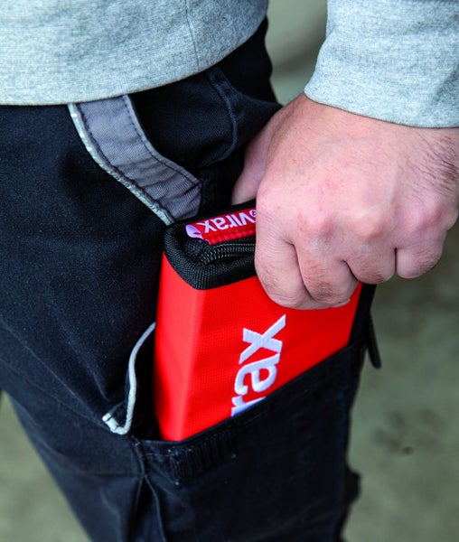 Eine Person verstaut eine rote Virax Werkzeugtasche in ihrer Hosentasche.