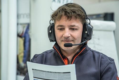 Mann mit Kapselgehörschutz inklusive Headset und Mikrofon in einer Arbeitsumgebung beim Lesen von Unterlagen.