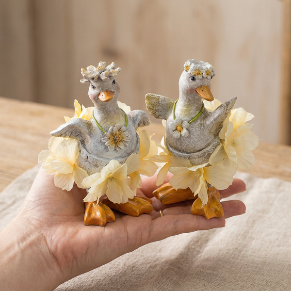 Zwei dekorative Entenfiguren mit Blumenkranz und gelben Stoffblüten, Frühlingsdekoration.