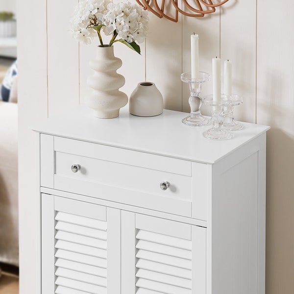 Weißer Badezimmerschrank mit Schublade und Lamellentüren, dekoriert mit Vasen, Kerzen und einem Spiegel