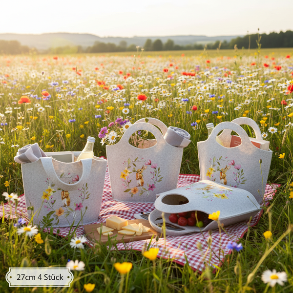Set aus vier grauen Filztaschen mit Hasenmotiv auf einer Picknickdecke in einer hellen Blumenwiese, Größe circa 27 Zentimeter.