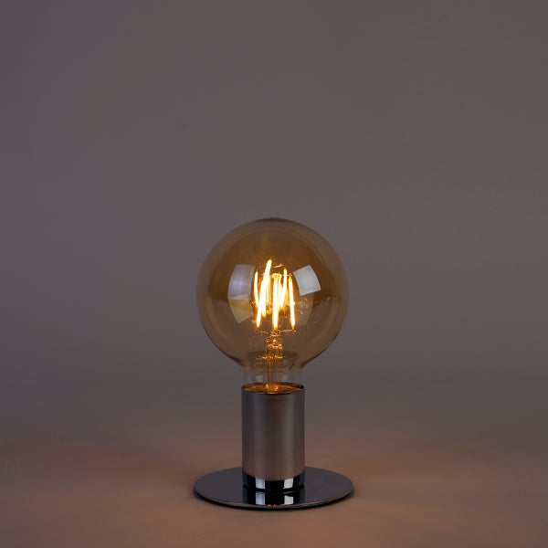 Tischleuchte mit verchromtem Metallsockel und einer großen, leuchtenden LED-Filament-Globelampe mit getöntem Glas.