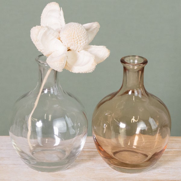 Zwei bauchige Glasvasen aus Klarglas und braunem Glas, eine mit einer weißen Trockenblume dekoriert, auf einer hellen Holzoberfläche.