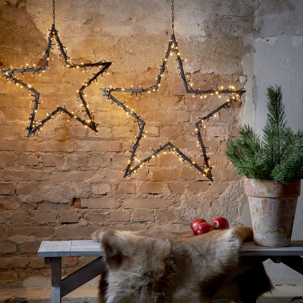 Dekorative Szene mit zwei hängenden Sternen, beleuchtet mit Lichtern an einer Ziegelwand