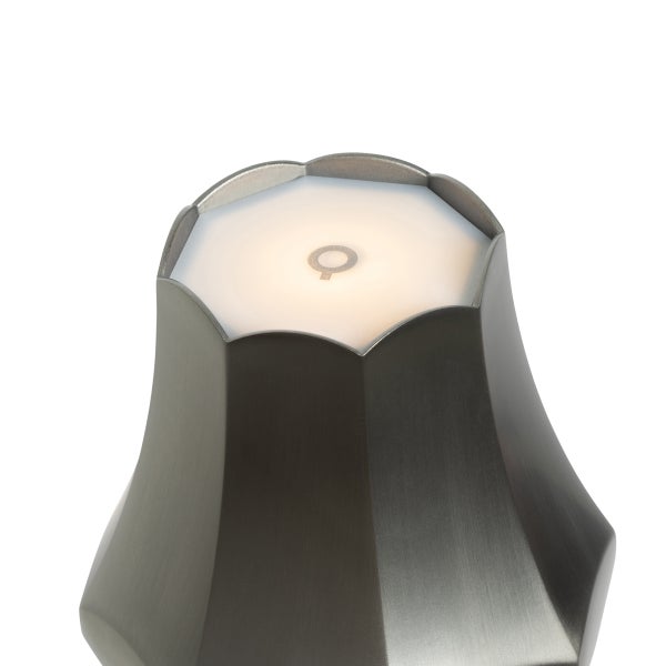 Detailansicht der Oberseite einer modernen Leuchte aus gebürstetem Metall mit beleuchtetem Q-Logo auf einer weißen Fläche.