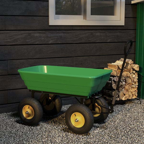 Grüner Gartenwagen mit vier Rädern und Handgriff auf Kies vor einer Holzwand mit Brennholz.