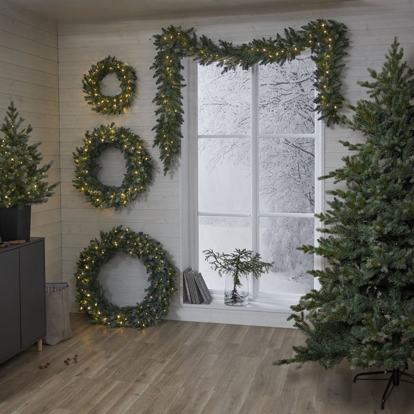 Festlich dekorierter Raum mit Weihnachtsbäumen, Kränzen und Girlanden.