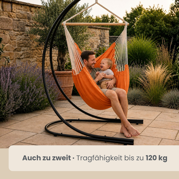 Vater und Kind sitzen gemeinsam in einem Hängesessel mit schwarzem Metallgestell auf einer Terrasse im Garten.