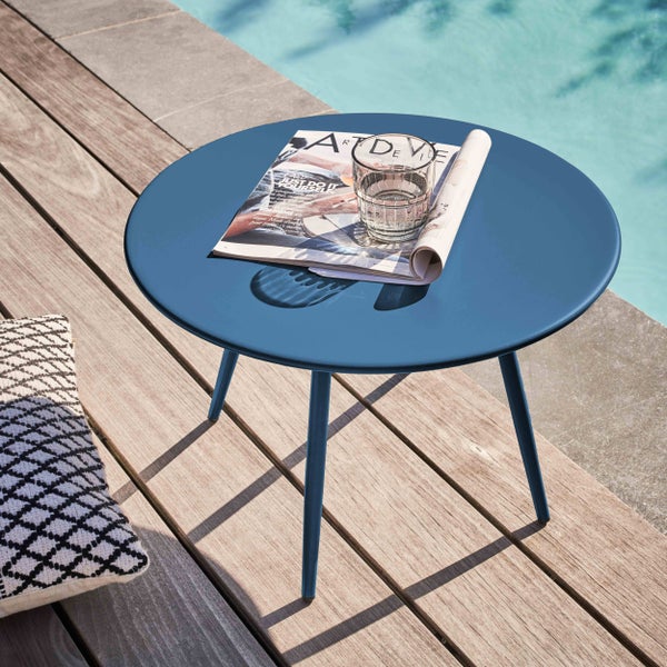 Runder Beistelltisch aus Metall in Blau auf einer Holzterrasse am Pool mit einer Zeitschrift und einem Glas Wasser.