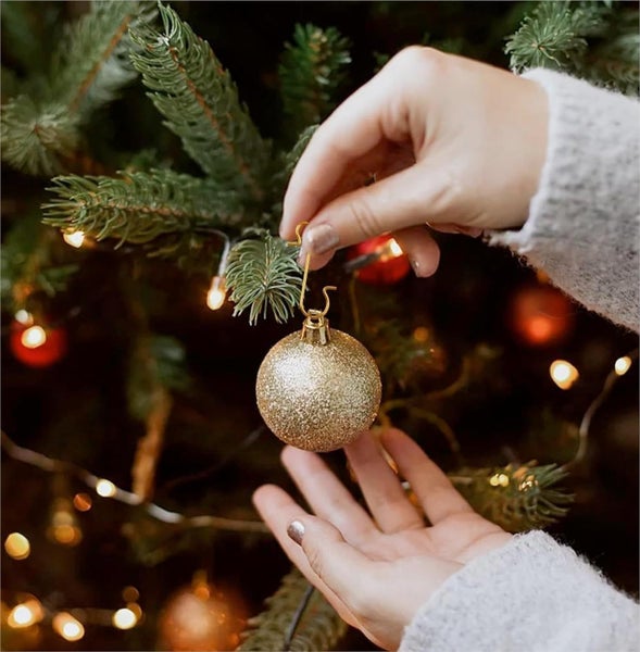 Person hängt glitzernde Weihnachtskugel an einen Weihnachtsbaum