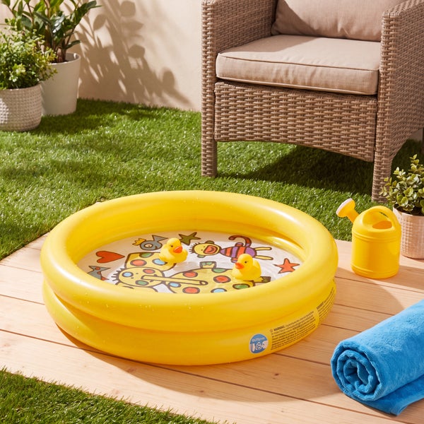 Aufblasbares Planschbecken für Kinder mit zwei Badeenten, auf einer Holzterrasse neben einem Gartenstuhl platziert.