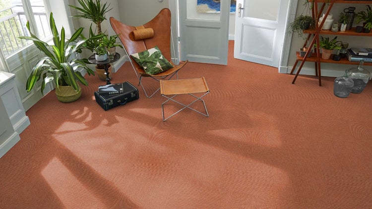 Moderner Wohnraum mit rötlichen Teppichfliesen in Schachbrettmuster, Leder-Sessel, Zimmerpflanzen und hellem Lichteinfall.