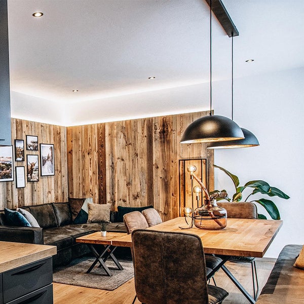 Helles Wohnzimmer mit Holzwand, Ecksofa und Esstisch mit Pendelleuchten