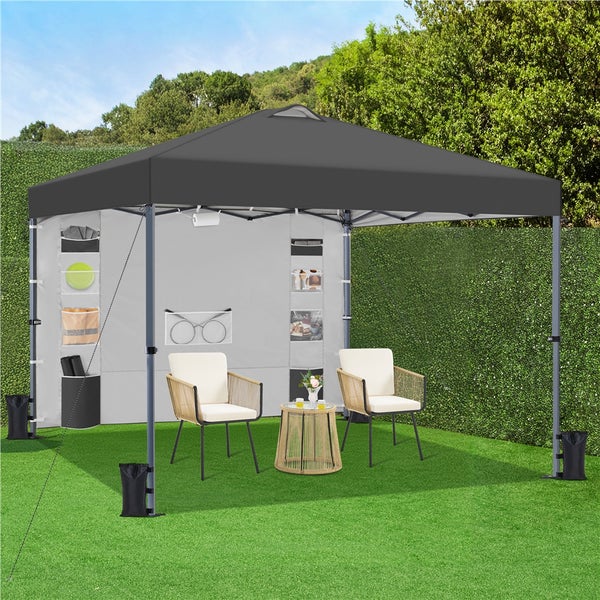 Grauer Pavillon mit Seitenwänden, Stühlen und Tisch im Garten.