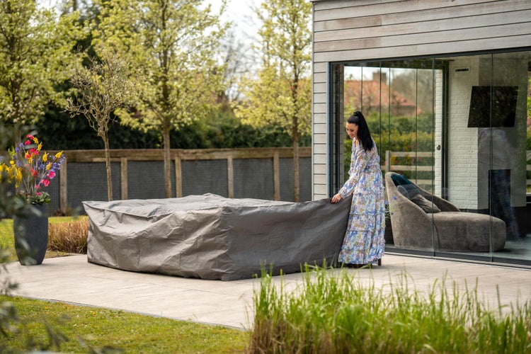 Gartenmöbel mit grauer Schutzhülle auf einer Terrasse, eine Frau im Hintergrund