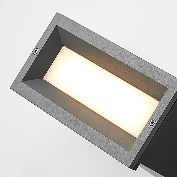 Detailansicht einer rechteckigen LED-Außenwandleuchte aus grauem Metall mit eingeschaltetem warmweißem Licht.