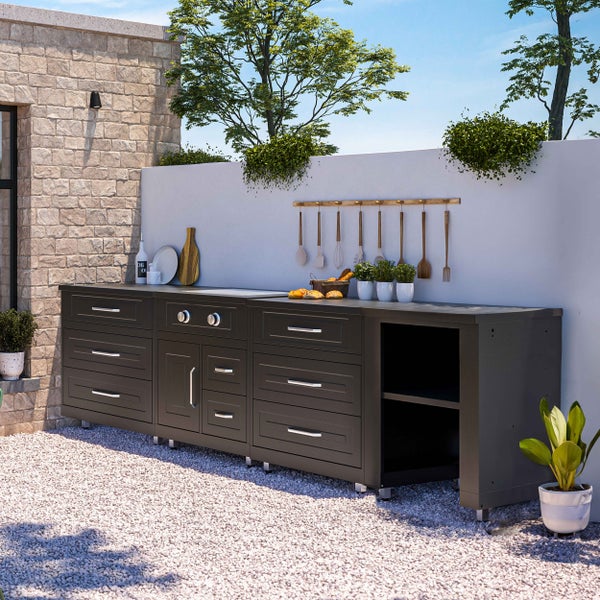 Moderne Außenküche in Anthrazit mit Schubladen, Schränken und integriertem Kochfeld in einem hellen Garten mit Steinmauer und Kiesboden.