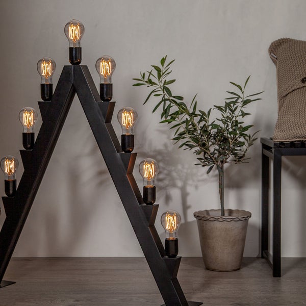 Dekorative Treppenleuchte mit mehreren Glühbirnen und einem Metallrahmen in Treppenform neben einer Zimmerpflanze.
