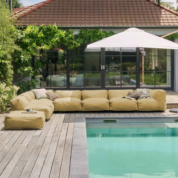 Modernes modulares Lounge-Sofa in Blau auf einer hellen Terrasse mit Holztisch und Meerblick, gestaltet im minimalistischen Stil.