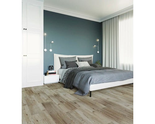 Modernes Schlafzimmer mit Laminatboden in Holzoptik, weißem Bett, grauer Bettwäsche, dunkelblauer Akzentwand und hellen Vorhängen.