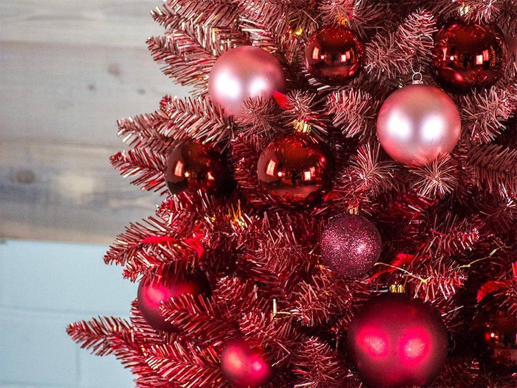 Detailansicht eines kunstlichen Weihnachtsbaums mit glänzenden und matten Weihnachtskugeln in verschiedenen Rotnuancen.