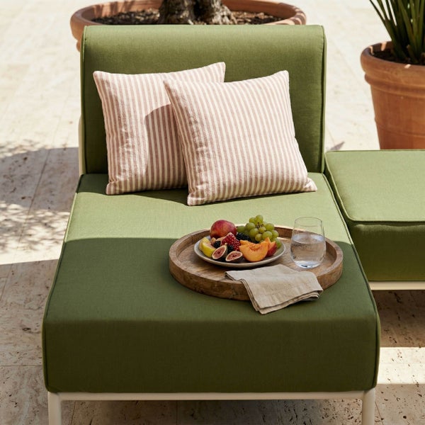 Grüner Polstersessel mit gestreiften Kissen und einem Holztablett mit Obst und Wasserglas auf einer Terrasse.