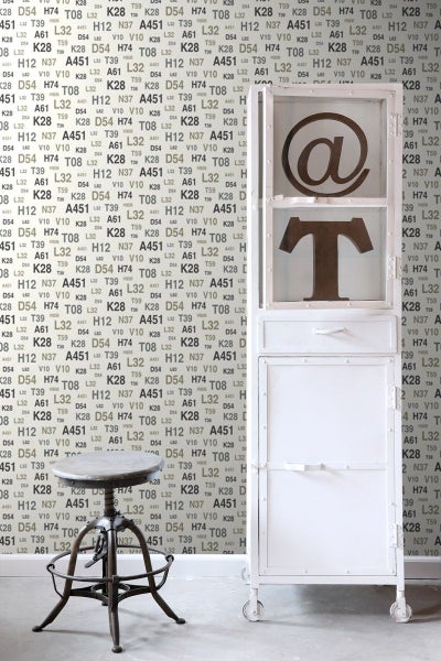 Szene mit einem weißen Schrank mit Fächern, einem Barhocker und einer gemusterten Tapete