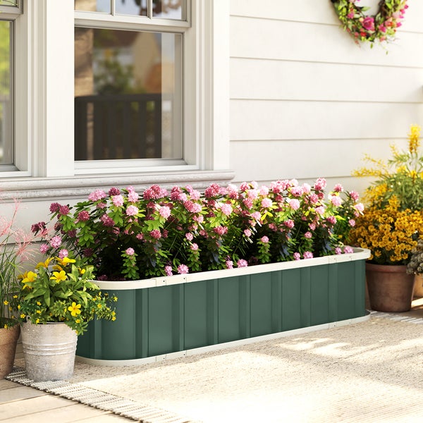Grünes Hochbeet aus Metall mit rosa Blumen vor einer weißen Hauswand auf einer Terrasse.