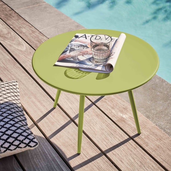 Runder lindgrüner Metall-Beistelltisch auf einer Holzterrasse am Pool mit einer Zeitschrift und einem Glas Wasser.