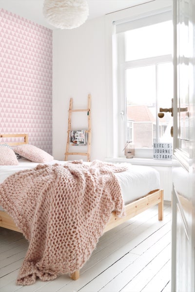 Helles Schlafzimmer mit Holzbett, Strickdecke, Leiterregal und geometrischer Tapete