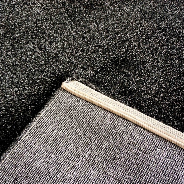 Nahaufnahme eines anthrazitfarbenen Teppichs mit flauschiger Oberfläche und gewebter Rückseite.