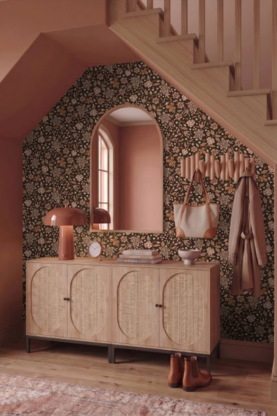 Moderner Eingangsbereich unter einer Treppe mit floraler Mustertapete, Sideboard mit Wiener Geflecht, Bogenwandspiegel und Tischleuchte.