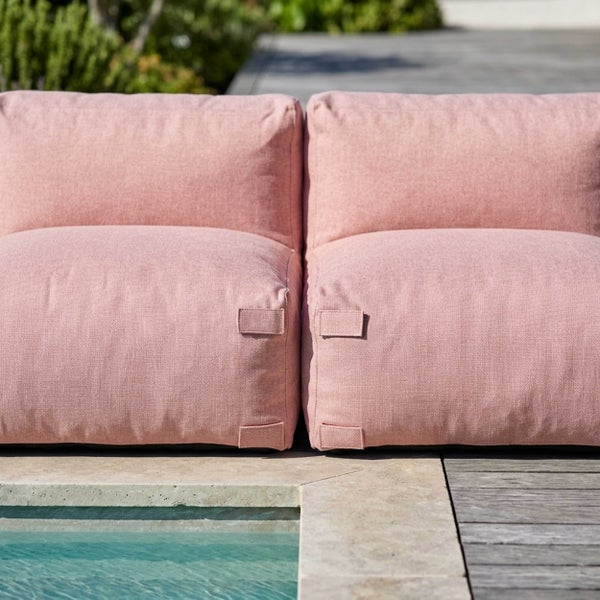 Zwei rosa Outdoor-Lounge-Sessel aus Stoff nebeneinander auf einer Stein- und Holzterrasse an einem Pool.