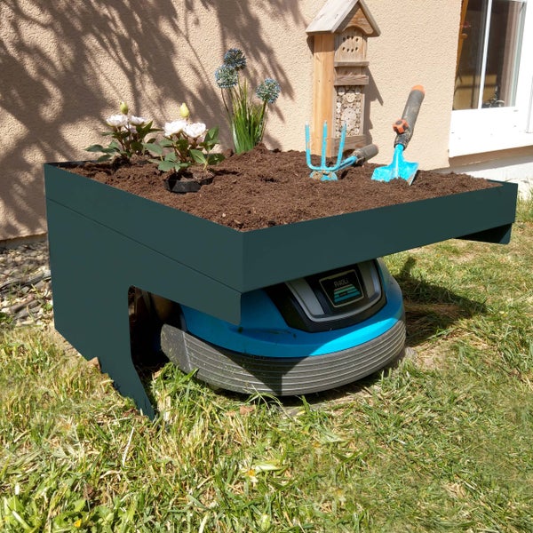 Szene mit einem Rasenmähroboter unter einem Pflanztisch, der mit Erde, Pflanzen und Gartengeräten dekoriert ist