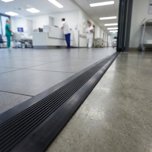 Profilschiene als Bodenübergangsprofil in einem Krankenhausflur, installiert zwischen Fliesenboden und Betonboden für einen barrierefreien Übergang.